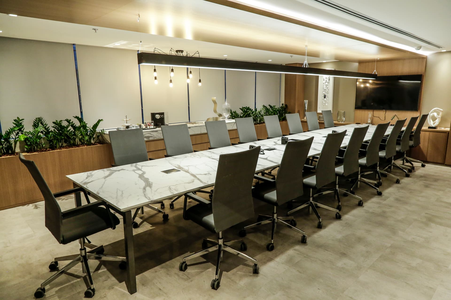 Sala de reuniões da JK Capital com longa mesa de mármore branco, cadeiras e plantas